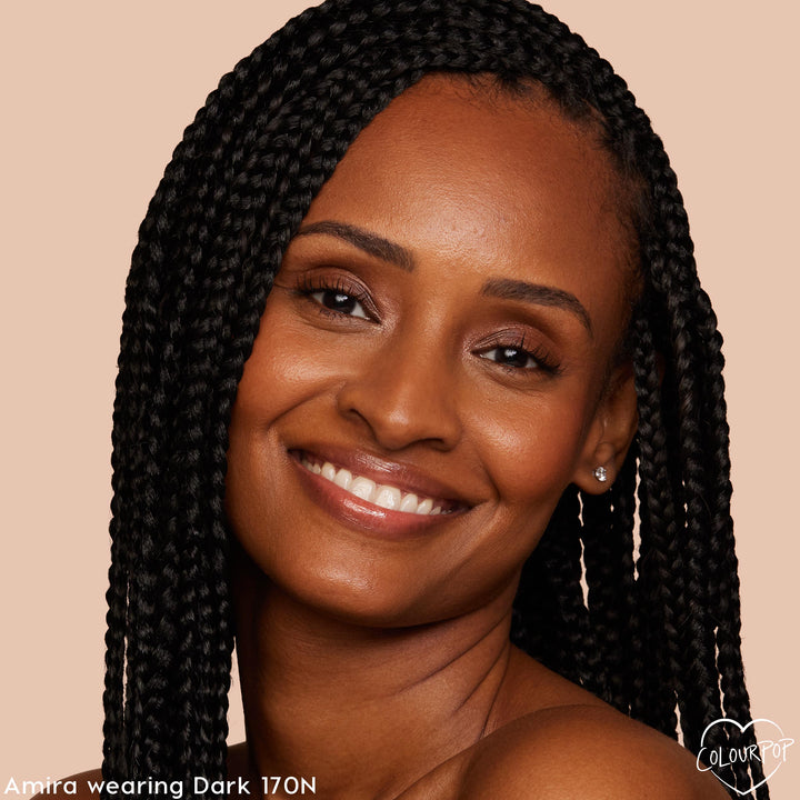 ColourPop Hyaluronic Hydrating Foundation in Dark 170 N worn by a smiling model, showing smooth, dewy medium coverage with a neutral undertone; close-up studio portrait with braided hair against a warm beige background.