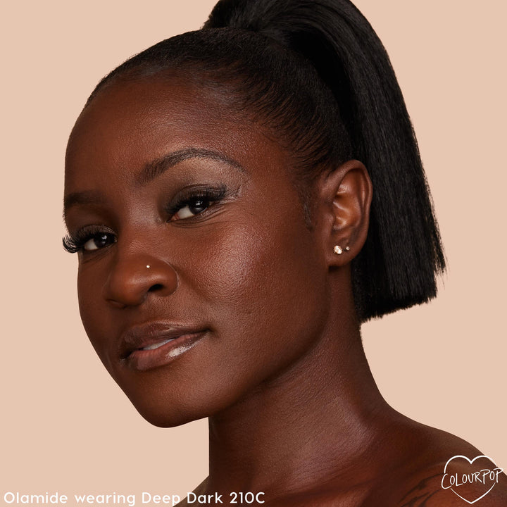 Deep Dark 210 C shade worn on a model’s face, showcasing smooth, dewy medium coverage with a warm undertone; ColourPop Hyaluronic Hydrating Foundation in a close-up studio portrait against a beige background with soft glam eye and glossy lips.