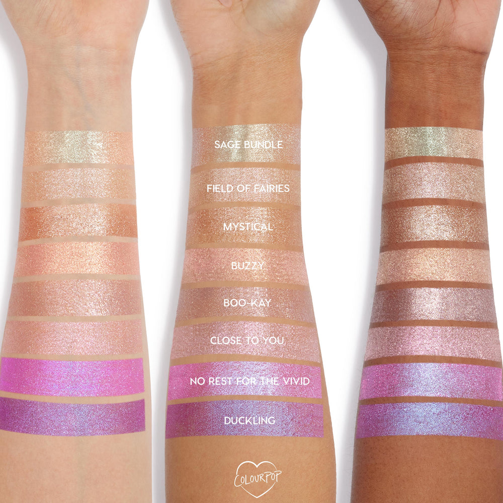 Buzzy Jelly Much Shadow swatched on three arms, showing a peachy rose-gold shimmer stripe among labeled shades; the ColourPop Jelly Much Shadow jelly-gel eyeshadow reflects metallic sparkle across light to deep skin tones.