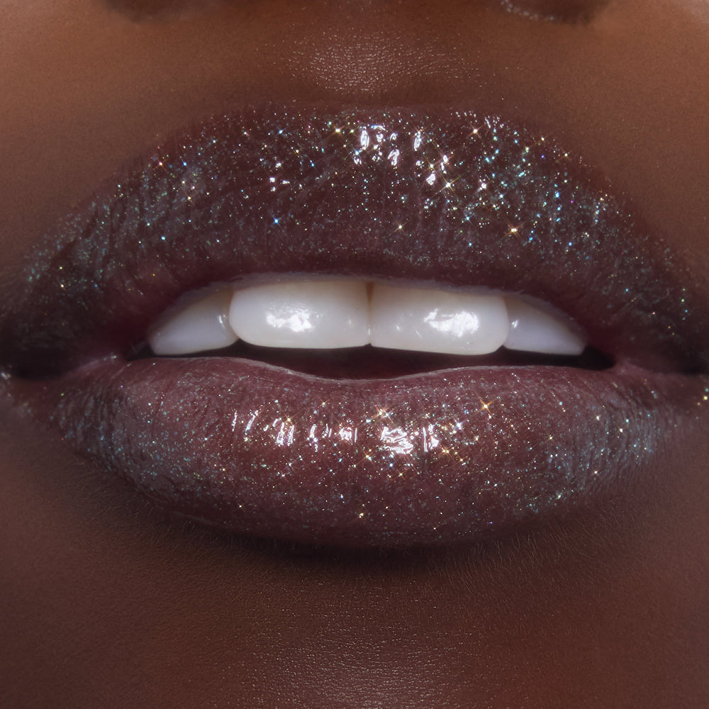 Lips wearing ColourPop Ultra Glossy Lip in Ogre, catching light with multi-dimensional shimmer and glassy shine as teeth gently show; studio macro highlights the deep plum base packed with fine glitter.
